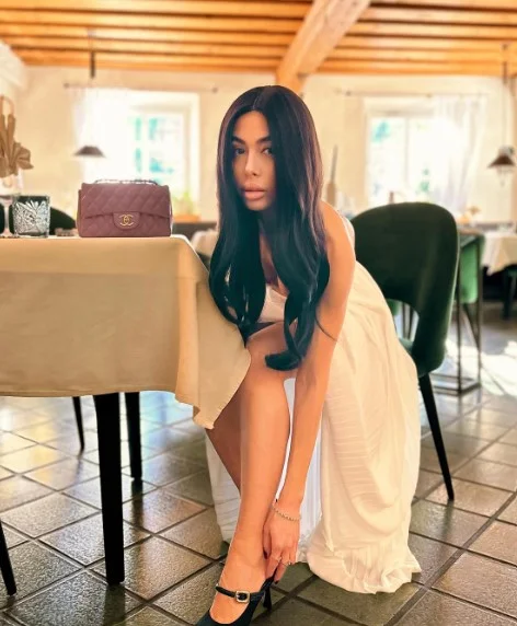 Virginia Olivero, modella OnlyFans, foto seduta su una sedia con un vestito bianco.